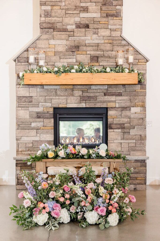 Sweetheart table surrounded by colorful wildflowers beside the stone fireplace