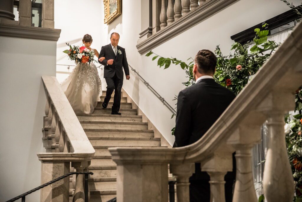 Kaori walking down the museum staircase with her father as Brian waits