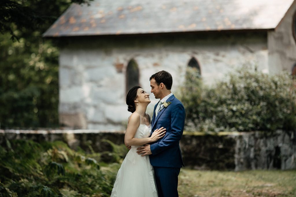 Caroline and Arthur smiling together beside a small stone chapel
