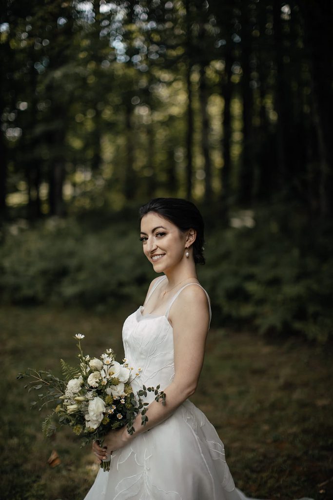 Caroline holding an ivory and green bouquet in the woods at Dexter’s Inn