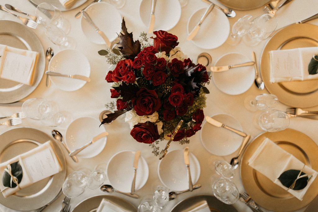 Deep-red wedding flowers surrounded by gold chargers and white place settings