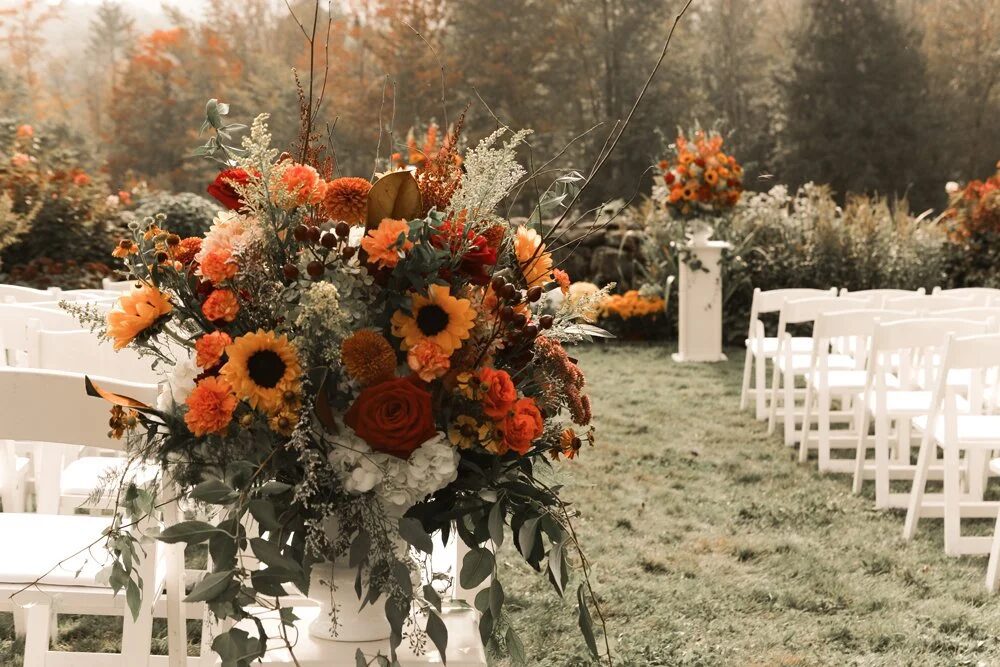 Orange fall flowers decorating an outdoor ceremony aisle at The Barn at Moody Mountain in Moultonborough, New Hampshire