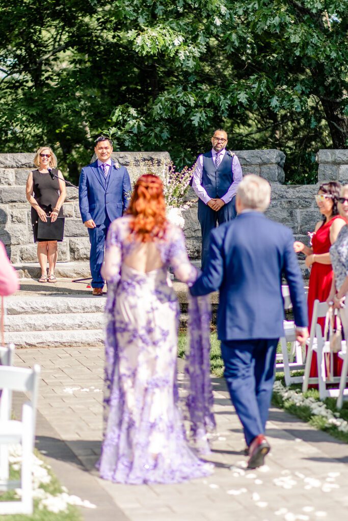 Bride in a purple wedding dress walking along a petal-lined aisle at Searles Castle in Windham, New Hampshire