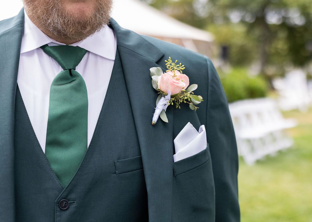 Forest green three-piece groom’s suit with matching tie and floral boutonniere