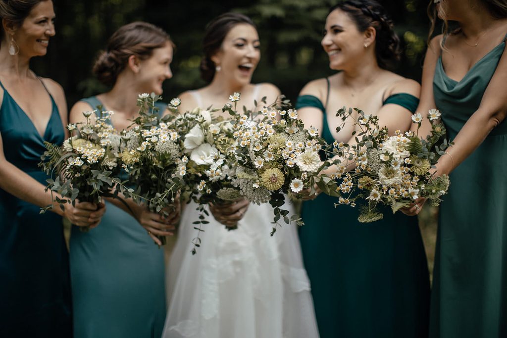 Bridesmaids in sage and hunter green dresses holding garden-style bouquets