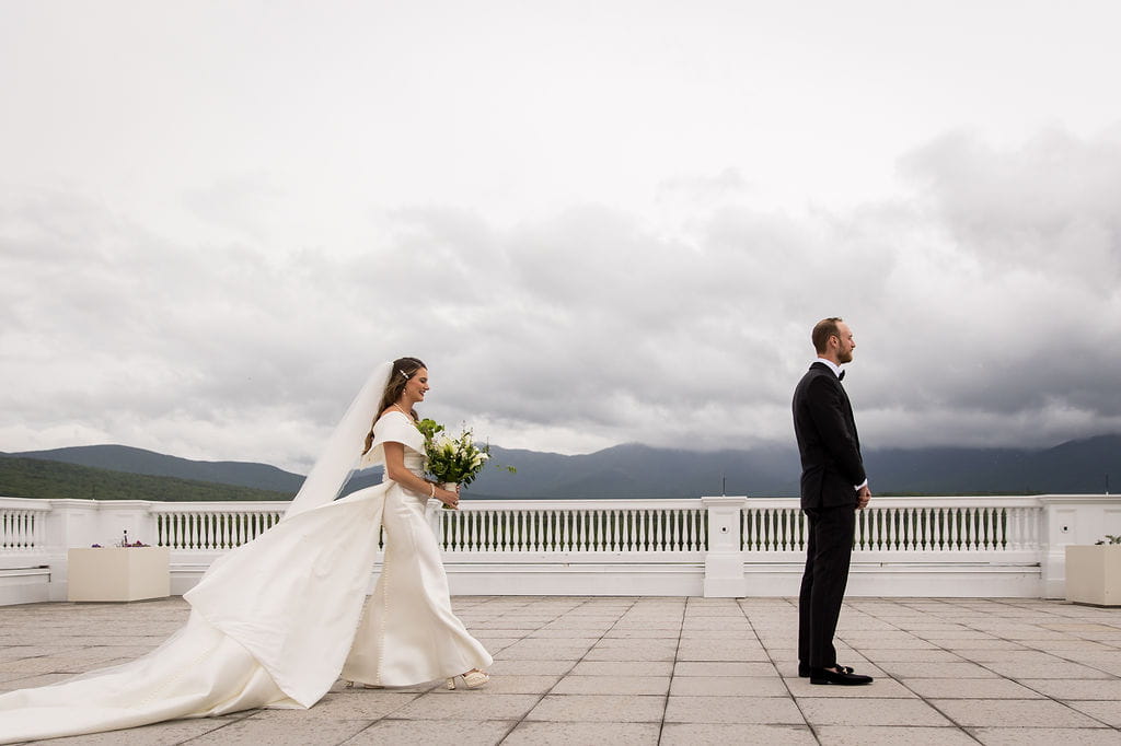 Katie approaching Alex for their first look with cloudy White Mountain views