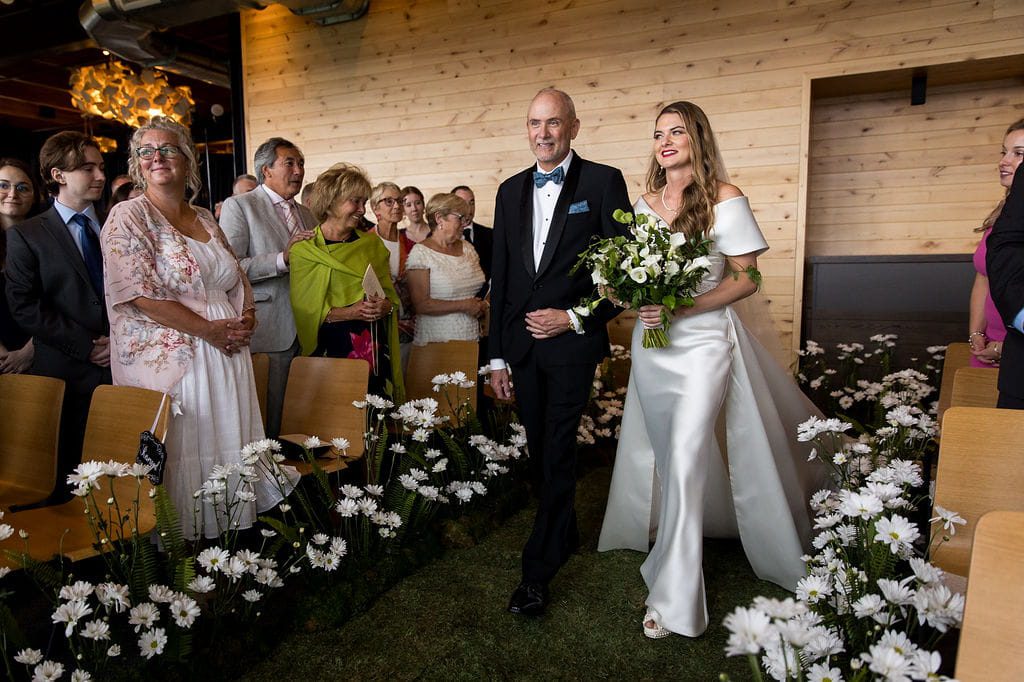 Katie walking down the moss aisle lined with white daisies at Rosebrook Lodge