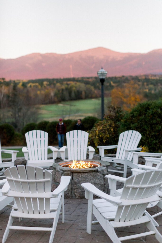 Adirondack chairs surrounding a fire pit with the White Mountains at sunset