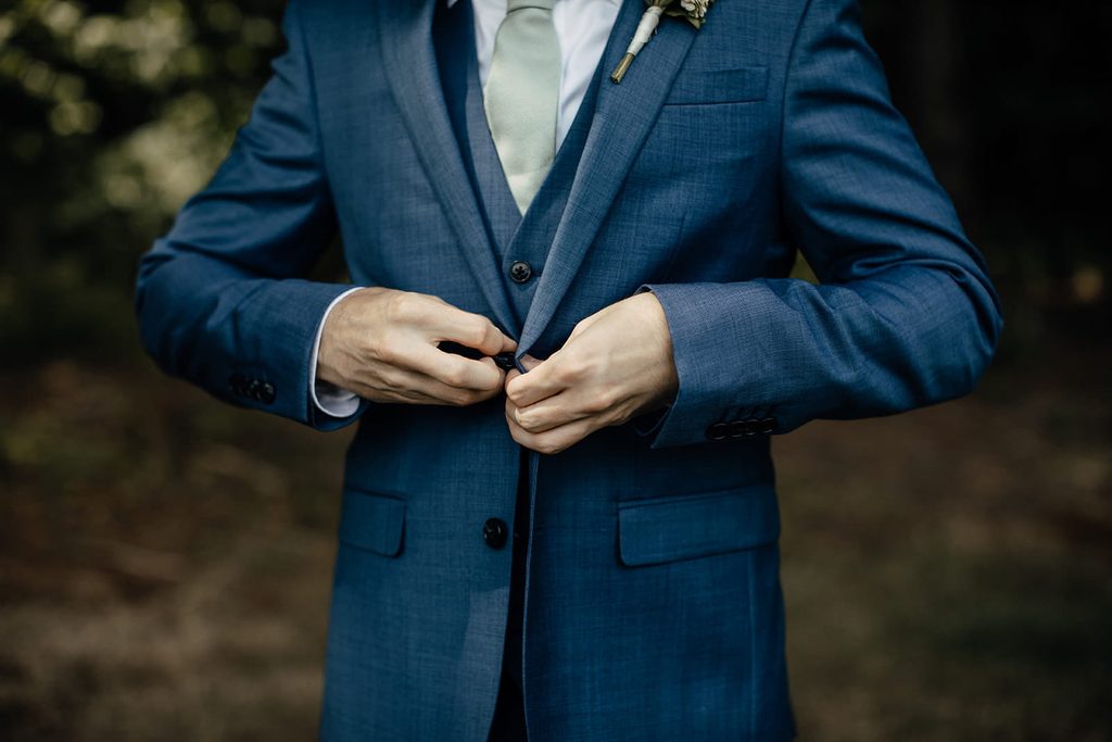 Arthur buttoning his navy wedding suit with a sage green tie