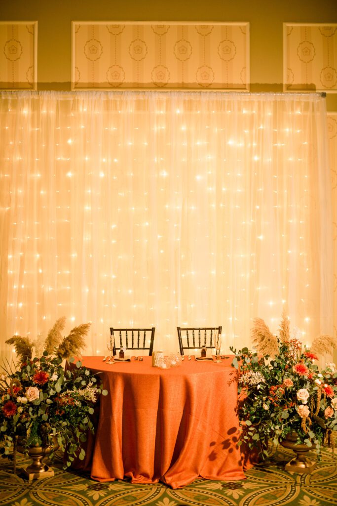 Burnt orange sweetheart table with flowers and a glowing light backdrop