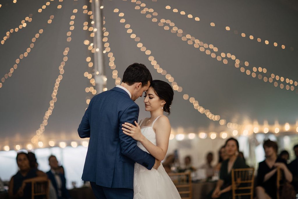 Caroline and Arthur dancing beneath warm string lights at their tented reception