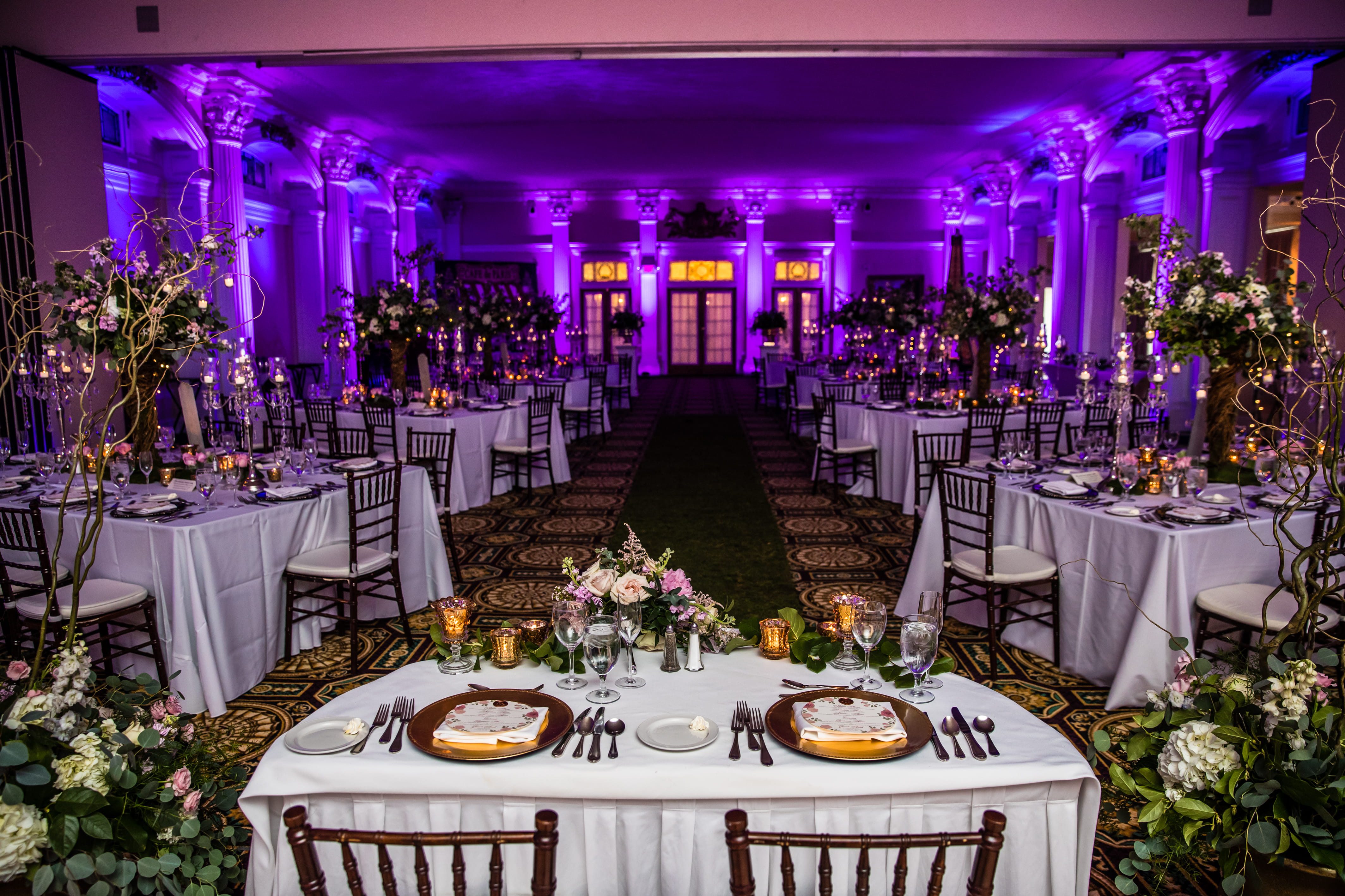 Candlelit wedding reception with pink flowers, greenery and purple uplighting