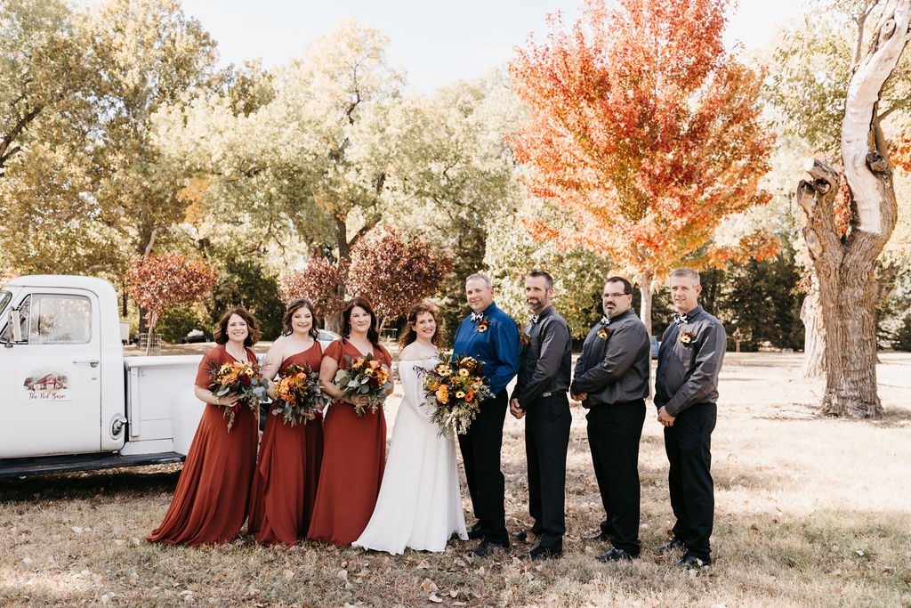 Mixed wedding party wearing rust dresses and coordinated dark separates at an outdoor New England wedding