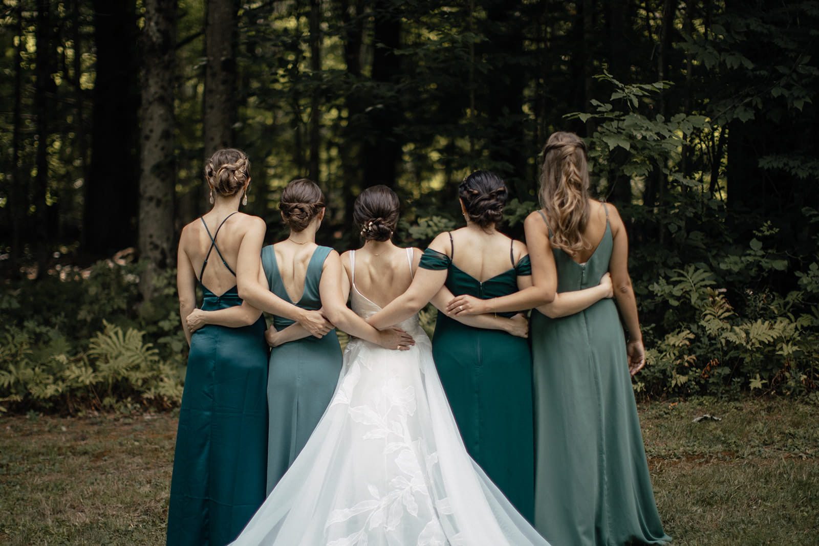 Caroline with bridesmaids wearing different shades of green in the woods