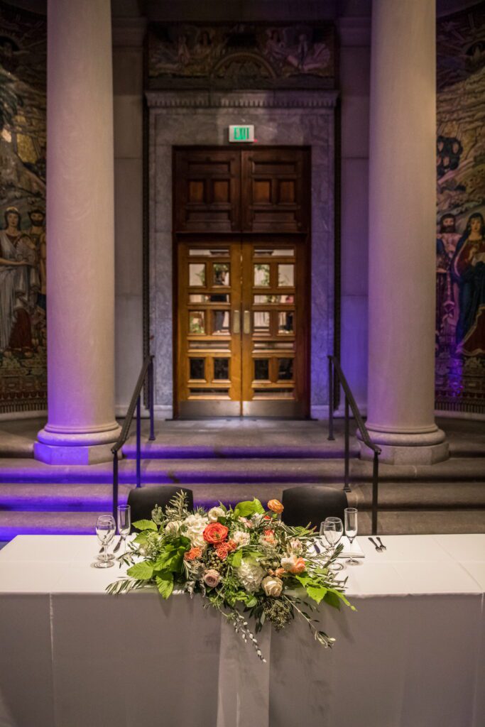 Floral sweetheart table beneath the columns and murals at the Currier Museum